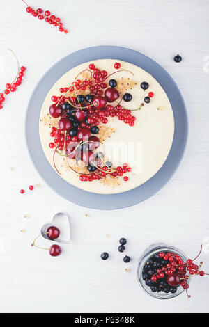 Homemade New York cheese cake with berries on white wooden table. Top view. Red currant, black currant and cherry. Stock Photo