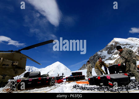 Chief Warrant Officer 3 Kirk Donovan (left) and Sgt. Jose Meza-Rangel, B Company, 1st Battalion, 52nd Aviation Regiment offload equipment and supplies from a CH-47F Chinook helicopter after landing on Kahiltna Glacier. Three crews from the U.S. Army Alaska Aviation Task Force spent the week in Talkeetna, Alaska, training in high altitude flying through the Alaska Range. The mission for Sunday, April 24, included continuing a longstanding partnership with the National Park Service to shuttle equipment and supplies to the Park Service base camp on Kahiltna Glacier for the upcoming climbing seaso Stock Photo