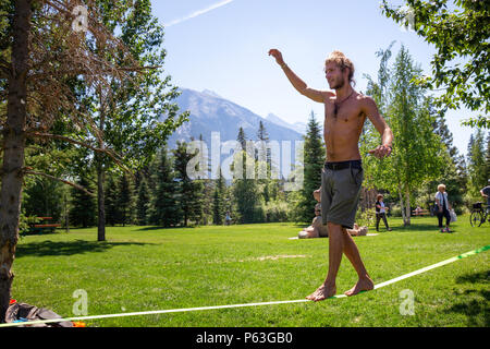 Banff, Alberta, Canada - June 20, 2018:  Adventurous man walking on a slackline in a park. Stock Photo