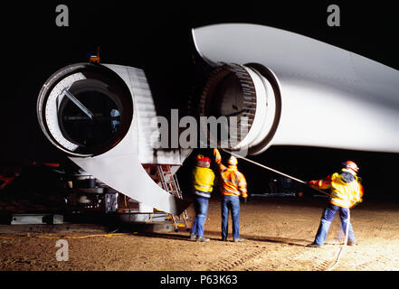 Long expopsure shot at night as three workers guide a blade into the hub of a giant Enercon wind turbine. Worksop United Kingdom. December 2008.
