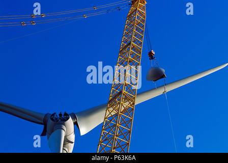 Two workers wait on the hub of a giant Enercon wind turbine ready to guide the nose cone that is being lifted into place. Worksop United Kingdom. Dece