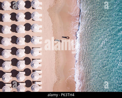 Aerial view of amazing turquoise sea with white umbrellas and sun loungers. Two people are walking on the shore. Beautiful sunny summer day in Sardini Stock Photo