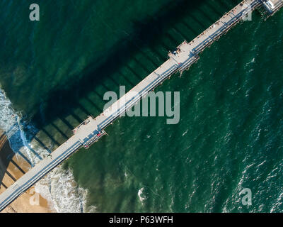 An aerial shot at 330 feet/100 meters looking down on a Southern California pier located on a small peninsula. White foam from crashing waves and vibr Stock Photo