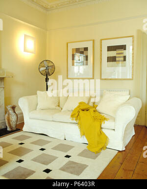 Pictures above white sofa with yellow wool throw in modern living room with check patterned rug Stock Photo