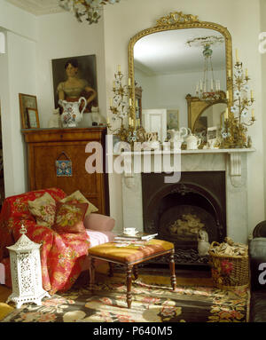 Antique gilt mirror above fireplace with antique candelabras in living room with red throw on armchair Stock Photo