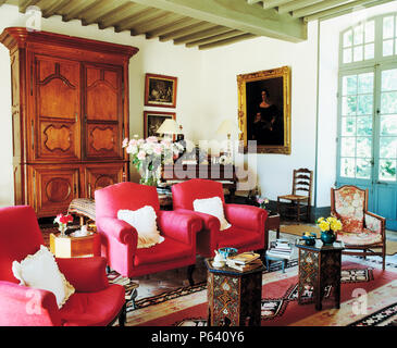 Deep pink armchairs and antique cupboard in French country living room with a pair of Moroccan inlaid side tables Stock Photo