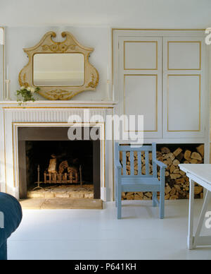 Ornate wooden mirror above fireplace in contemporary living room with white flooring and painted blue chair Stock Photo