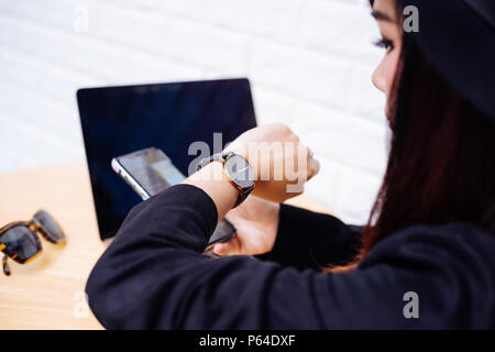 Young fashionable business woman looking at watch, waiting for someone with a mobile phone and laptop. Late for appointment concept Stock Photo