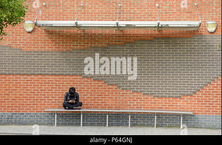 Guy sitting cross legged on bench. Nice graphic wall behind. Stock Photo