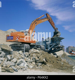 Fiat-Hitachi FH200 excavator loading concrete into mobile crusher for recycling. Stock Photo