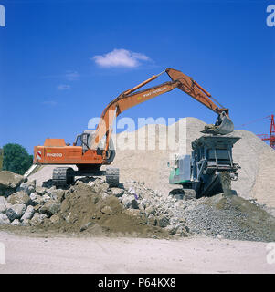 Fiat-Hitachi FH200 excavator loading concrete into mobile crusher for recycling. Stock Photo