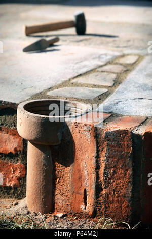 An improvised plant pot made from a section of old clay soil pipe built into a patio laid with natural stone slabs, UK Stock Photo