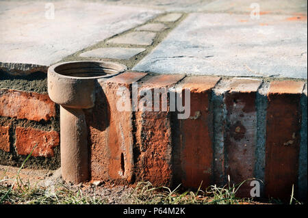 An improvised plant pot made from a section of old clay soil pipe built into a patio laid with natural stone slabs, UK Stock Photo