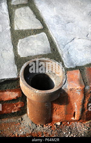 An improvised plant pot made from a section of old clay soil pipe built into a patio laid with natural stone slabs, UK Stock Photo