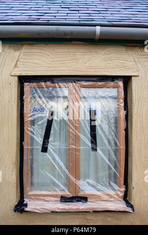 Plastic sheeting to mask off new hardwood casement windows while a cottage under renovation is rendered, UK Stock Photo