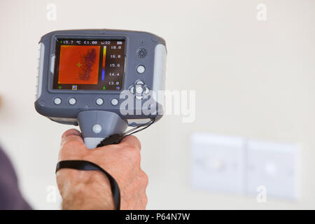 A technician uses a thermal imaging camera to check heat loss around light switchs in a house. Stock Photo
