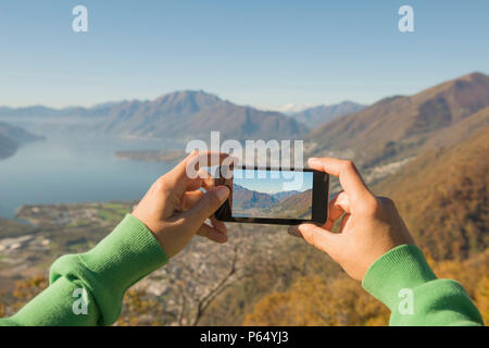Woman Taking a Photo of the Mountain and Alpine Lake Maggiore with Mobile Phone in Ticino, Switzerland. Stock Photo