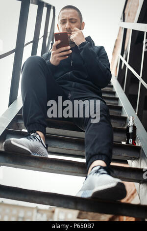 Young man sitting on a ladder and watching his mobile phone. Stock Photo