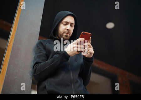 Bearded man standing next to concrete post and staring at the screen. Stock Photo