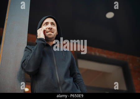Bearded man standing next to concrete post and talking by phone. Stock Photo