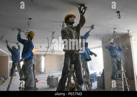 Chinese workers sanding ceiling plaster in a new office tower in Beijing. Stock Photo