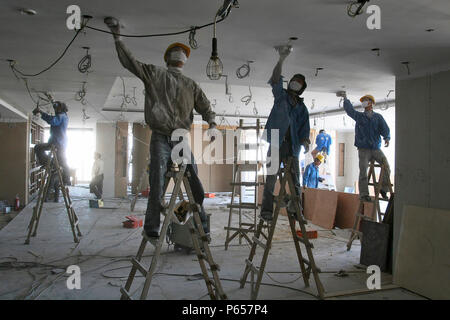 Chinese workers sanding ceiling plaster in a new office tower in Beijing. Stock Photo