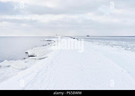 White snow lies on the mole to the red lighthouse at the mouth of the Daugava in winter in Latvia Stock Photo