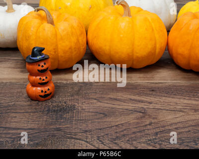 Three orange miniature ceramic pumpkin heads wearing black hat with white, yellow, and orange pumpkins on background over dark wooden surface with space used in Halloween, festival, and decoration Stock Photo