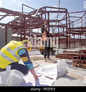 Workers on site guiding a crane driver with engineer looking at building plans. Stock Photo