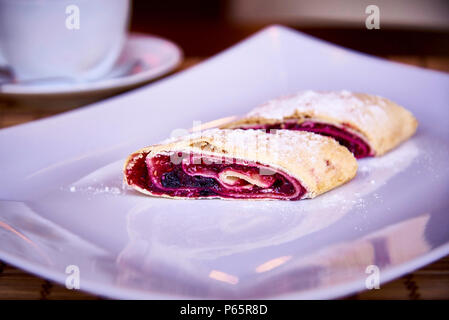 Appetizing strudel with berries on a white plate with powder and a cup on a saucer close-up. Stock Photo