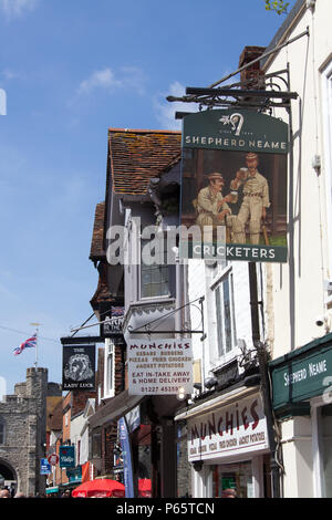 City of Canterbury, England. Picturesque street view of pub and shops on Canterbury’s High Street, with the historic West Gate in the background. Stock Photo