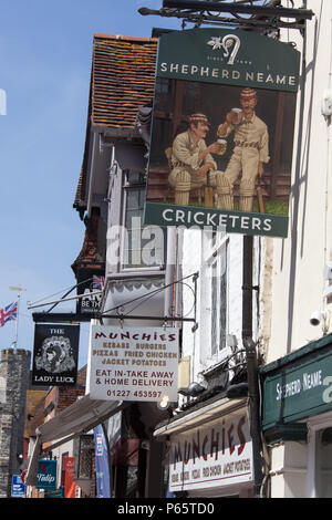 City of Canterbury, England. Picturesque street view of pub and shops on Canterbury’s High Street, with the historic West Gate in the background. Stock Photo