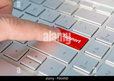 A finger press a button with text support on laptop keyboard. support inscriptions on the grey silver keyboard button close up. Red button. Stock Photo