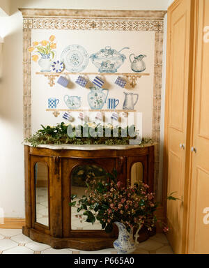Close-up of trompe-l'oeil shelves with crockery painted above antique marble-topped cupboard with mirrored doors