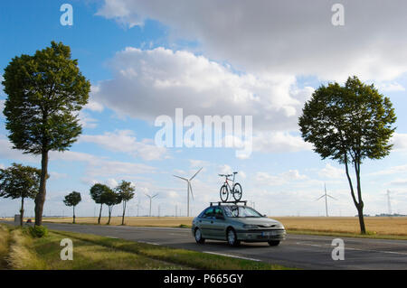 Car with bicycle on roof driving past wind farm near Etampes, France Stock Photo