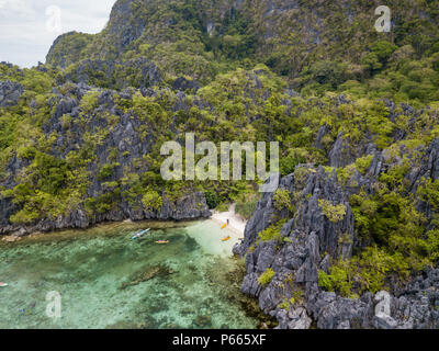 Aerial drone view of boats around a tiny sandy beach on a tropical island surrounded by towering limestone cliffs Stock Photo