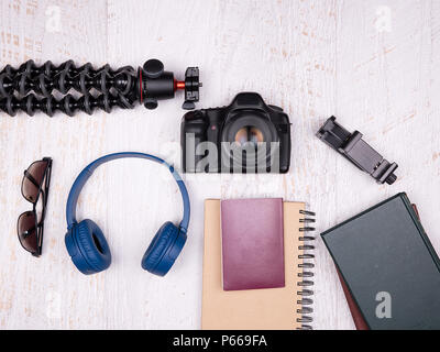 Flat lay top view of traveler accessories on white wooden background. DSLR and action camera, blue headphones, passport, tripod, flash, laptop and sma Stock Photo