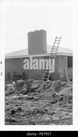 Black and white photograph, showing a newly constructed, single story, brick-faced tract house, with dirt and building debris in the yard, and a wooden ladder leaning on the side of the house next to a large rectangular chimney stack, likely photographed in Ohio, August, 1956. () Stock Photo