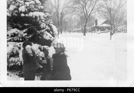 Black and white photograph, showing a warmly-dressed, blonde woman, crouching down, with a raised hand open to catch a snowball about to be thrown by a small, warmly clothed boy in front of her, with snow-covered ground, trees, and houses, visible in the background, likely photographed in Ohio in the decade following World War II, 1950. () Stock Photo