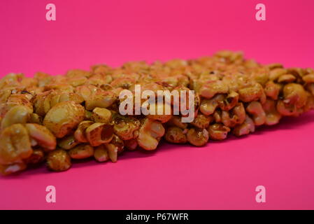 On a bright colorful pink paper background is located and placed from a delicious and sweet grilling of air corn kernels, popcorn with caramel Stock Photo