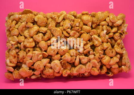 On a bright colorful pink paper background is located and placed from a delicious and sweet grilling of air corn kernels, popcorn with caramel Stock Photo