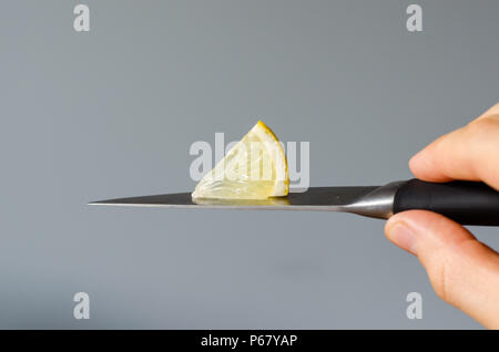 A piece of lemon on on a knife blade in hand. close-up Stock Photo