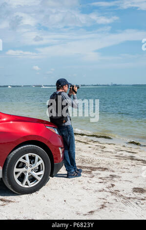 man leaning on a car taking photographs of the Gulf of Mexico with a DSLR camera Stock Photo