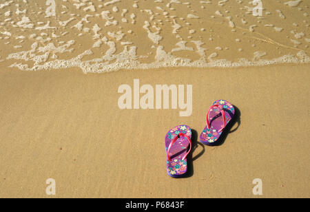 Pair of vibrant colored flip-flops or sandals on golden sand beach with the wave swash Stock Photo