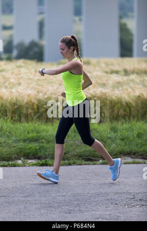 Young woman jogging, running, checking her vital signs on a fitness watch, fitness tracker, heart rate, number of steps, distance, time, calories burn Stock Photo