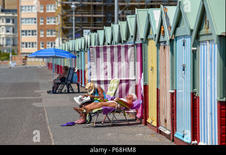 Hove Brighton UK 29th June 2018 - Sunbathers enjoy the beautiful hot sunshine by their beach huts on Hove  seafront as the heatwave continues throughout Britain Credit: Simon Dack/Alamy Live News Stock Photo