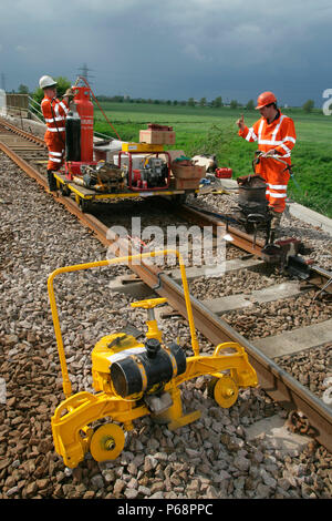 Trackworkers prepair to carry out thermit welding on newly laid track whith a rail grinding machine in the foreground. Peterborough. May 2005 Stock Photo