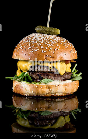 Manhattan burger - Spicy guacamole, crispy bacon, sun dried tomatoes and rocket lettuce with reflection isolated on black background Stock Photo