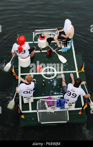 GERMANY, East Germany, Plau, floating mini football field with goal and german flags, four paddling fans in football jersey of German women soccer team and beer box, at funny boat contest and carnival like event Badewannenrallye engl. bathtub rallye, drinking Luebzer beer a brand of Carlsberg Stock Photo