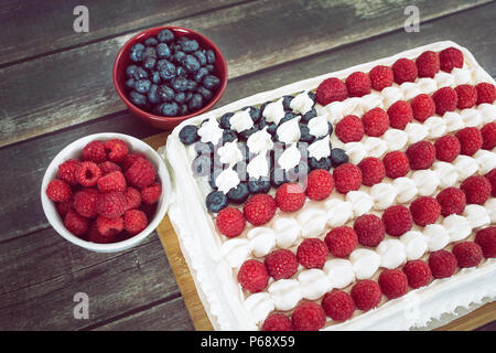 Patriotic, red white and blue, American flag cake with fresh raspberries and blueberries on rustic wooden table. Stock Photo